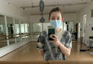 A dancer in a mask takes a selfie in the mirror of a dance studio.