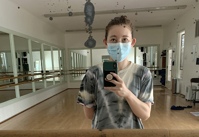 A dancer in a mask takes a selfie in the mirror of a dance studio.