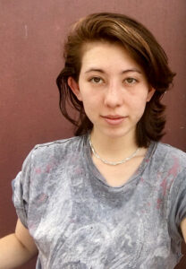 Erin looks into the camera wearing a gray t shirt against a brown backdrop.