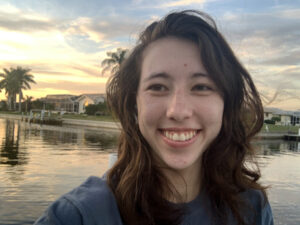 Erin smiles in front of palm trees and a water front.