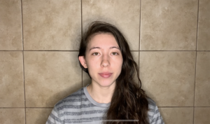 A dancer with long brown hair over her shoulder lays on brown tile floor.