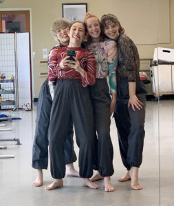 Four dancers smile and pose in a mirror.