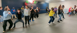 A large group of people take a dance in a dance studio.
