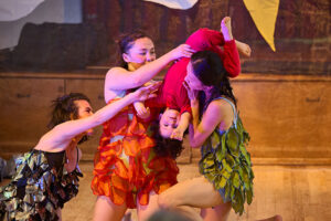 Three dancers onstage lift a toddler in red upside down.