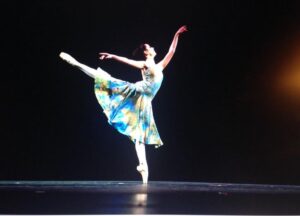 Sydney in arabesque onstage wearing a blue dress.