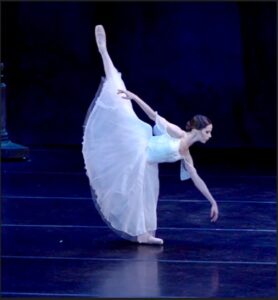 Sydney in a penchee arabesque onstage wearing a long white skirt.
