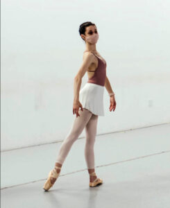 A dancer in tendu arabesque in a studio wearing a mask.