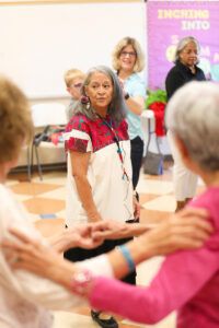 Lucy stands and coaches two dancers holding each other's arms.