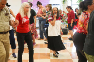 Lucy speaks into a microphone, guiding the dancers as they walk in twos in a circle around her.