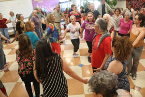 A big group of people hold hands and dance in a circle.