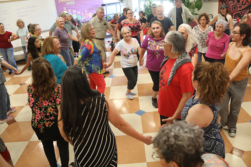A big group of people hold hands and dance in a circle.