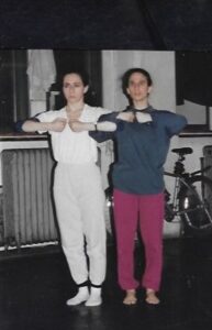 Two dancers stand and link arms in a studio