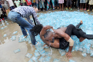 Three performers wrestle in a huge pile of small bags filled with water the feet of people in the crowd encircles them.