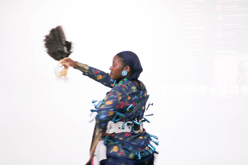Umi IMAN dances the Jingle Dress Dance against a white background, wearing a sacred regalia known as the Jingle Dress. IMAN’s dress, like others of its kind, is adorned with rows of metallic cones that create sound as she moves. The Jingle Dress Dance is a healing dance that originated with the Ojibwe people and is now embraced across many Native communities.