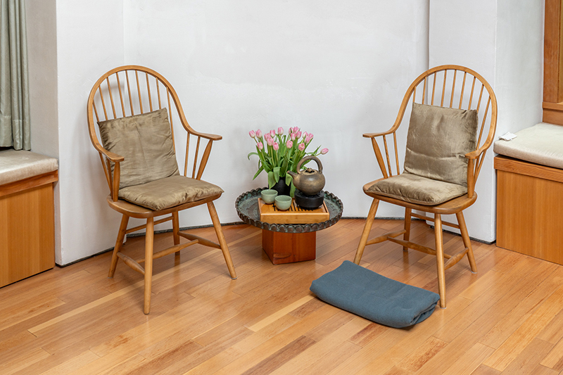 Copilot said: Two wooden spindle-back chairs with cushions face each other across a small round table holding a teapot, cups, and pink tulips, creating a simple, inviting conversation space on a hardwood floor.