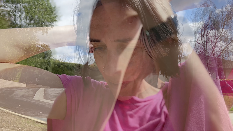 A layered double-exposure portrait combines a close-up figure in a pink shirt adjusting their hair with an outdoor landscape, blending human presence and environment into a reflective, dreamlike composition.